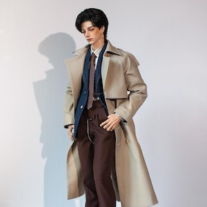 May include: A doll wearing a beige trench coat, a blue blazer, a striped tie, brown pants, and black shoes.