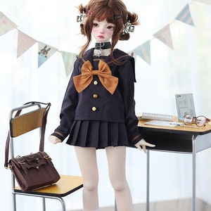May include: A doll wearing a black and brown school uniform with a brown bow tie, white socks, and black loafers. The doll is standing next to a small wooden desk and a chair.