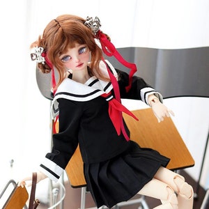 May include: A doll wearing a black sailor uniform with a red ribbon, black shoes, and white socks. The doll is sitting on a wooden chair with a brown bag hanging from the back.