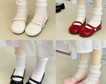 May include: Four pairs of doll shoes in white, red, black, and pink. Each pair has a strap across the foot and a small pearl accent. The shoes are worn by dolls with white socks.