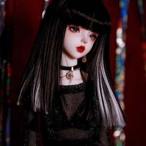May include: A black and white doll with long hair, wearing a black mesh top, a black choker necklace with a crystal pendant, and a gold chain belt. The doll has blue eyes and red lips.