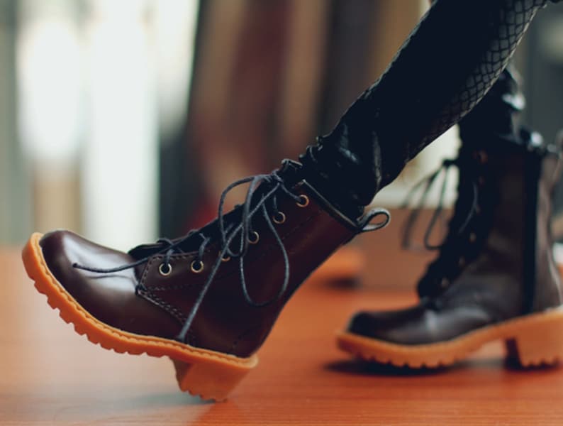 May include: A pair of brown leather boots with laces and a light brown sole. The boots have a small heel and are worn with black leggings. The boots are a classic style, suitable for various outfits.