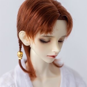 May include: A doll with long, auburn hair styled in a side braid. The doll is wearing a white shirt and has a neutral expression.