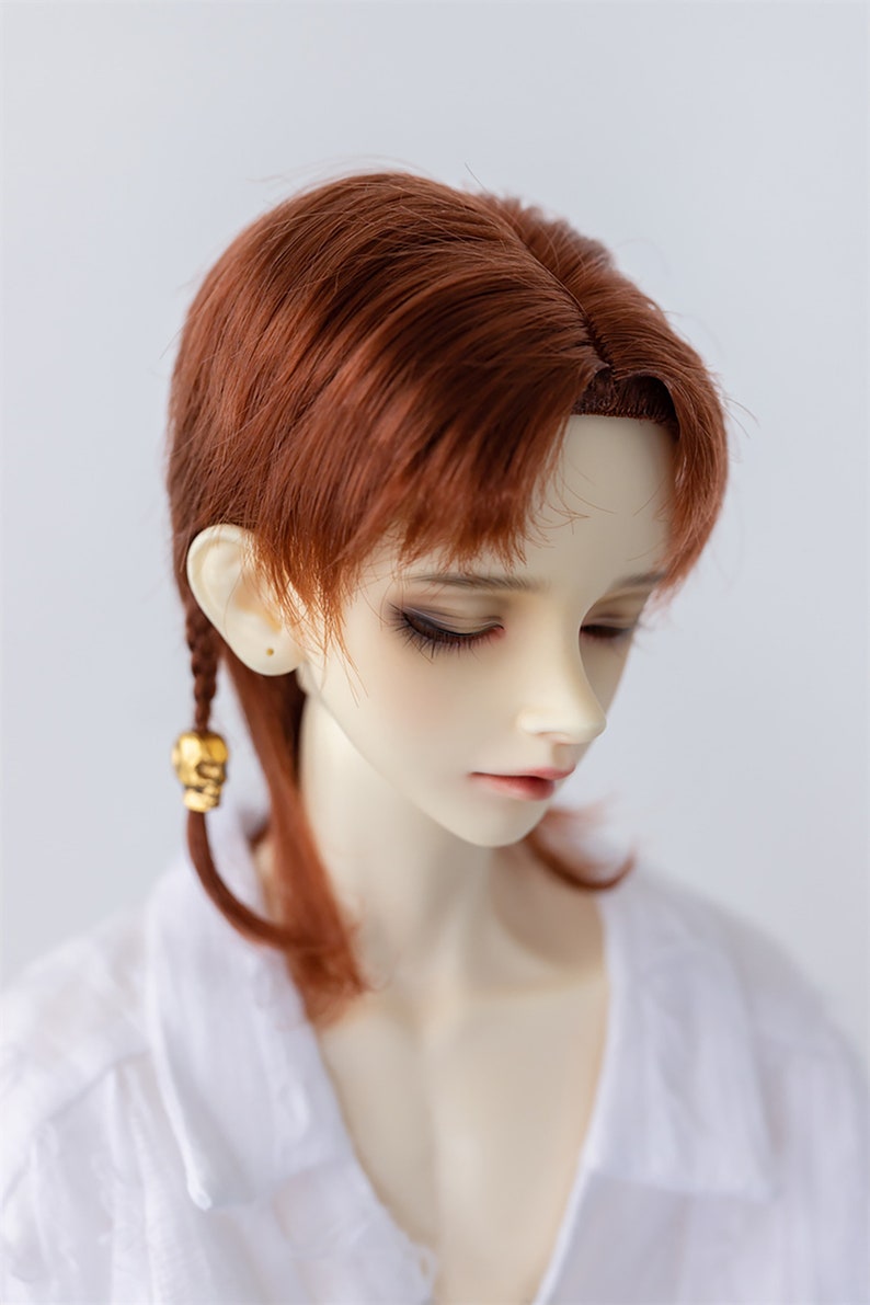 May include: A doll with long, auburn hair styled in a side braid. The doll is wearing a white shirt and has a neutral expression.