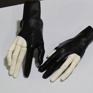 Op de afbeelding: Een paar zwarte vingerloze handschoenen met een uitgesneden ontwerp op de achterkant van de hand. De handschoenen zijn gemaakt van zacht, soepel leer.