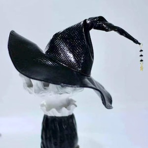 May include: A black witch's hat with a pointed crown and a wide brim. The hat has a textured surface and a gold chain with black beads hanging from the tip.