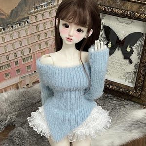 Puede incluir: Un su&eacute;ter de color azul claro y peludo con un borde de encaje blanco. El su&eacute;ter tiene un dise&ntilde;o de hombros descubiertos y un dobladillo ligeramente asim&eacute;trico.
