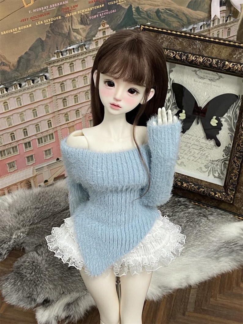 Puede incluir: Un su&eacute;ter de color azul claro y peludo con un borde de encaje blanco. El su&eacute;ter tiene un dise&ntilde;o de hombros descubiertos y un dobladillo ligeramente asim&eacute;trico.