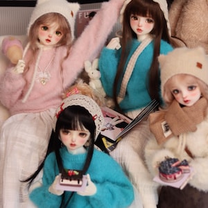 May include: A collection of fashion dolls wearing sweaters, hats, and skirts. The dolls are holding miniature accessories, such as a cake and a lollipop. The dolls are seated on a white surface.
