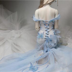 May include: A light blue dress with a lace-up back and butterfly embellishments. The dress has a long train and is made of a sheer fabric.