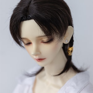 May include: A doll with long, dark brown hair styled in a side part with a braid on one side. The doll is wearing a white shirt and has a small earring in one ear.