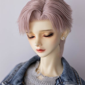 Könnte beinhalten: Eine Puppe mit einer hellrosa Perücke, die in einem kurzen, geschichteten Haarschnitt gestylt ist. Die Puppe trägt eine Jeansjacke über einem grauen Pullover.