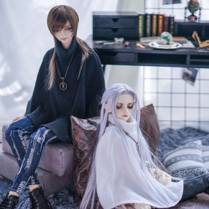 May include: Two dolls wearing sweaters and jeans. The doll on the left has brown hair and is wearing a black sweater and blue jeans. The doll on the right has white hair and is wearing a white sweater and black trousers.