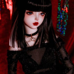 May include: A doll with long black hair and bangs, wearing a black off-the-shoulder top with a mesh overlay and a gold belt. The doll has blue eyes and red lips. The background is a red fabric with a blurry pattern of colorful lights.