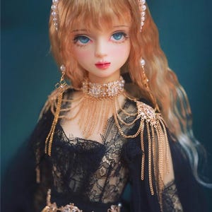 May include: A porcelain doll with blonde hair wearing a black lace dress and gold jewellery. The doll has blue eyes and a pearl headband.