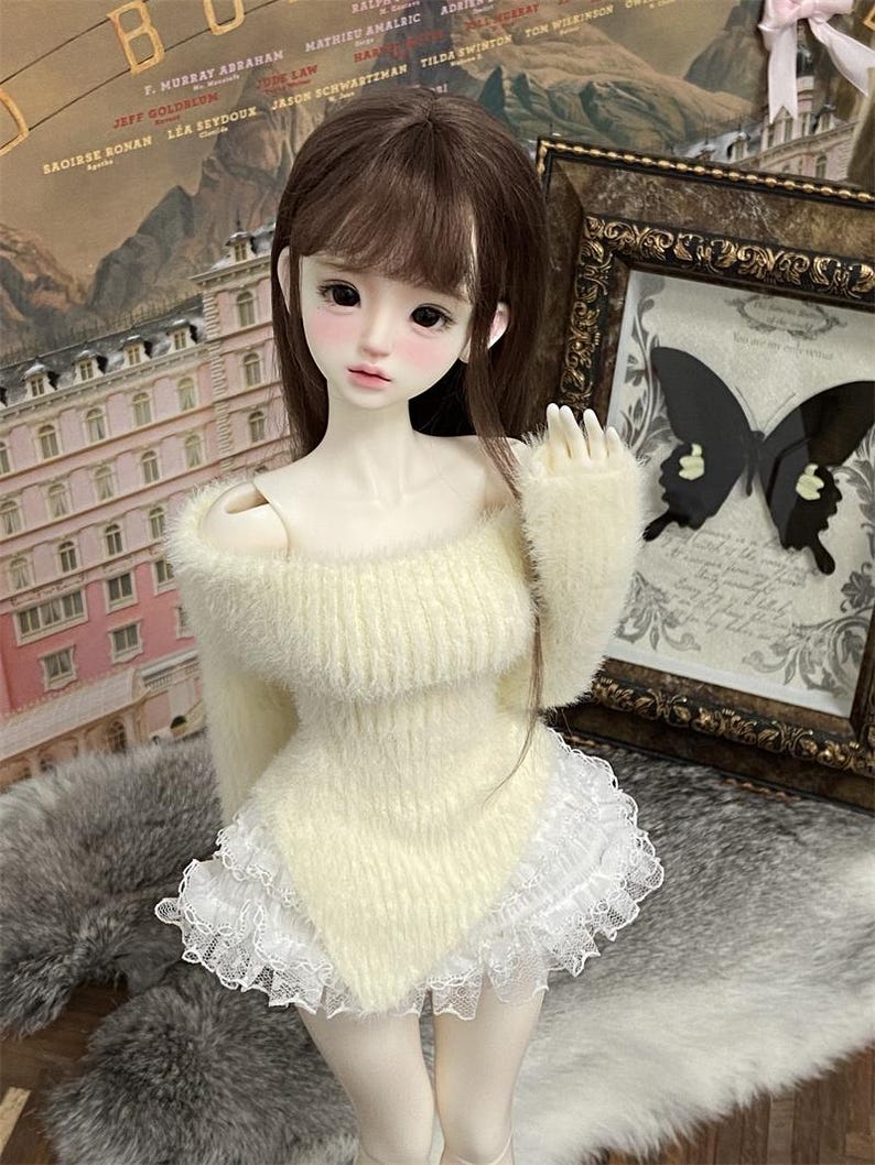 Puede incluir: Una mu&ntilde;eca de peluche blanco con un su&eacute;ter blanco peludo con un borde de encaje blanco. La mu&ntilde;eca tiene el pelo largo y casta&ntilde;o y lleva una falda de encaje blanco.