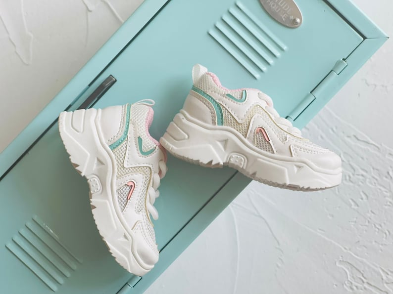 Puede incluir: Un par de zapatillas blancas con una parte superior de malla y una suela gruesa. Las zapatillas tienen detalles en rosa y verde.