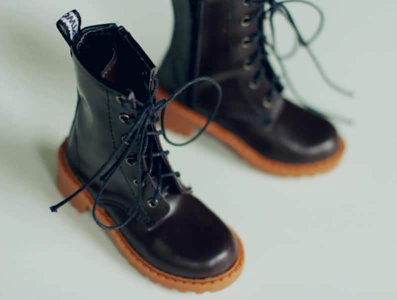 May include: A pair of dark brown leather boots with laces and a zipper. The boots have a round toe and a light brown sole. The boots are designed with a classic style.