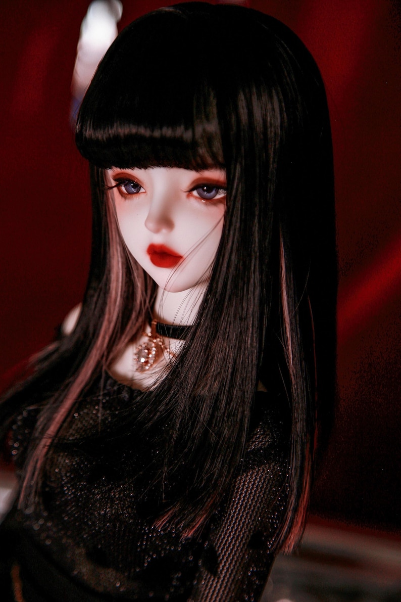 May include: A doll with long black hair with pink highlights, wearing a black mesh top and a silver necklace. The doll has a white face with red lips and blue eyes.