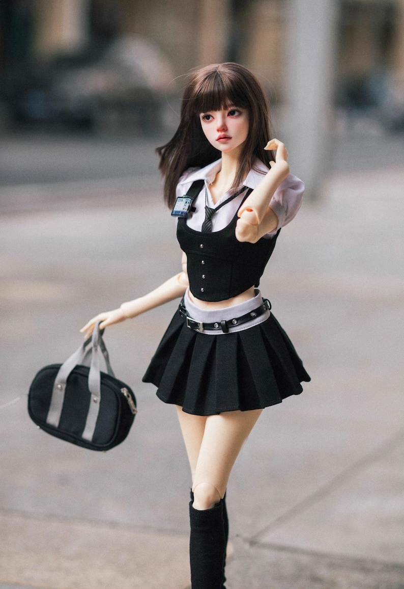 May include: A doll dressed in a school uniform, featuring a black pleated skirt, a black vest over a white collared shirt, and a black tie. The doll carries a black bag with gray straps and wears black boots.