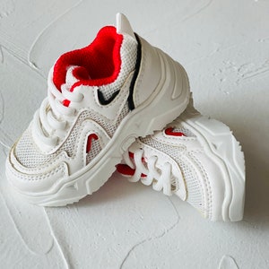 Puede incluir: Zapatillas blancas con detalles rojos y dise&ntilde;o de malla. Las zapatillas tienen una suela gruesa y cierre de cordones.