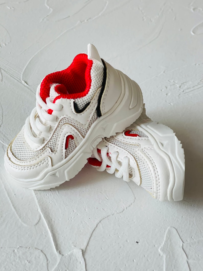 Puede incluir: Zapatillas blancas con detalles rojos y dise&ntilde;o de malla. Las zapatillas tienen una suela gruesa y cierre de cordones.