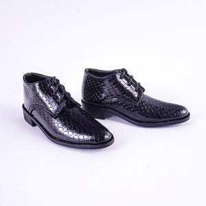May include: A pair of black leather shoes with a snakeskin pattern. The shoes have laces and a rounded toe.