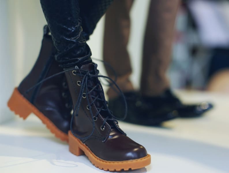 May include: Brown leather boots with orange soles and laces. The boots have a classic design with a round toe and a sturdy heel. The laces are dark blue and the boots are worn with dark pants.