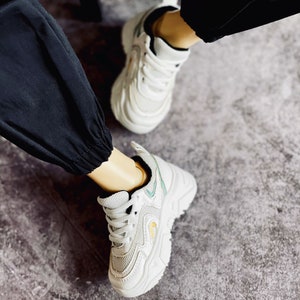 Puede incluir: Zapatillas blancas con suela gruesa y parte superior de malla. Las zapatillas tienen un dise&ntilde;o azul claro y amarillo en el lateral.