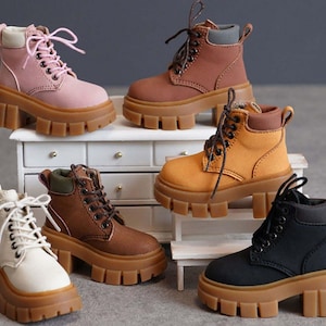 May include: A collection of six ankle boots featuring thick, chunky gum-colored lug soles and lace-up closures. The boots are available in various colors including light pink, brown, tan, cream, and black, each with matching laces and collars.