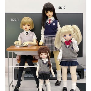 May include: Four dolls wearing school uniforms with grey sweaters and plaid skirts. The dolls are standing in front of a desk with a book on it. The text "SDGR" and "SD10" are visible in the image.