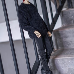 May include: A doll with red hair wearing a black fuzzy sweater, black trousers, and black combat boots. The doll is posed on a staircase, leaning against a black metal railing. The doll has a pale complexion and is wearing rings.