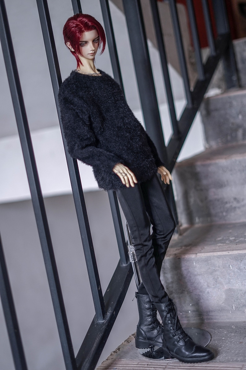 May include: A doll with red hair wearing a black fuzzy sweater, black trousers, and black combat boots. The doll is posed on a staircase, leaning against a black metal railing. The doll has a pale complexion and is wearing rings.