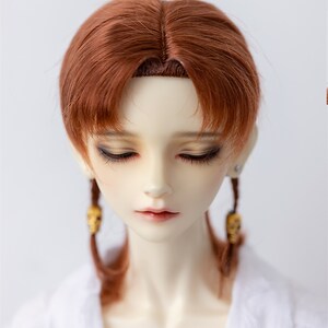 May include: A doll with long, auburn hair styled in two braids with skull-shaped charms. The doll is wearing a white collared shirt.