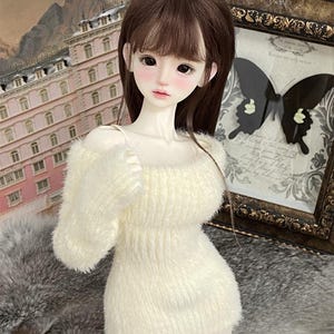 Puede incluir: Un vestido de su&eacute;ter blanco y peludo con cuello redondo y mangas largas. El vestido est&aacute; hecho de un material suave y esponjoso y tiene una silueta ligeramente ajustada.