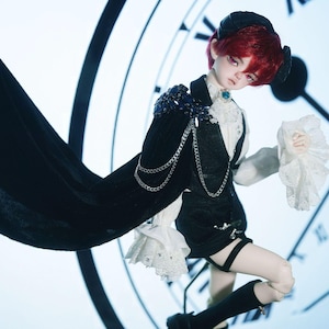 Puede incluir: Una muñeca con cabello rojo que lleva un atuendo blanco y negro con una capa y una cadena. La muñeca está de pie frente a una esfera de reloj.