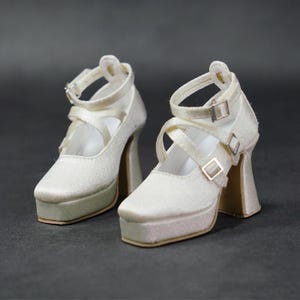 May include: A pair of white platform heels with criss-cross straps and buckles.