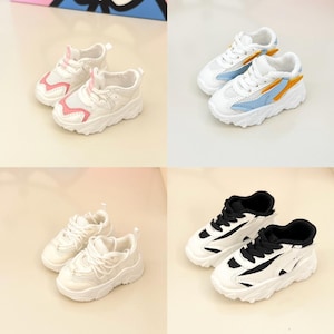 May include: Four pairs of white sneakers with different colored accents. The sneakers have a chunky sole and a mesh upper. The accents include pink, blue, yellow, and black.