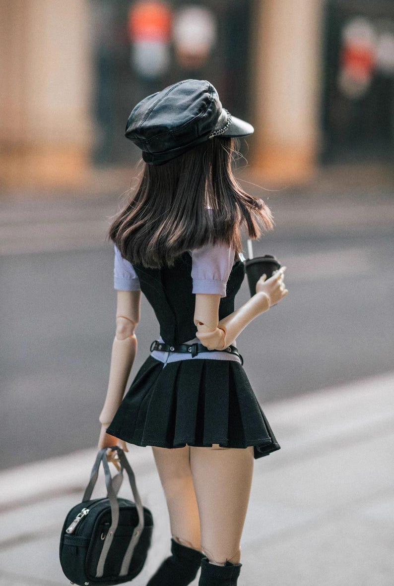 May include: A doll wearing a black leather cap, a black vest over a light purple shirt, and a black pleated skirt. The doll is holding a black bag and a black coffee cup. The doll is walking on a city street.