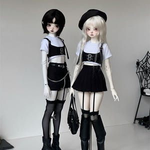 May include: Two fashion dolls wearing black and white outfits. The dolls are wearing black skirts, white shirts, and black boots. One doll is wearing a black beret and the other doll has black hair. Both dolls are wearing black and white stockings.