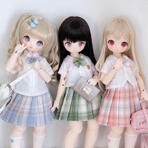 May include: Three dolls wearing school uniforms with plaid skirts. The doll on the left is wearing a light blue skirt, the doll in the middle is wearing a green skirt, and the doll on the right is wearing a pink skirt. Each doll has long hair and is holding a small accessory.
