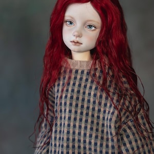 May include: A handmade doll with a pale complexion, blue eyes, and bright red hair. The doll is dressed in a sweater with a blue and beige checked pattern. The doll's outfit includes a blue skirt.