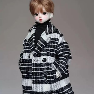 May include: A doll wearing a black and white striped coat with a black turtleneck underneath. The doll has short brown hair and blue eyes.