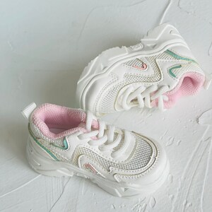 Puede incluir: Zapatillas blancas de malla con ribetes rosas y suela blanca. Las zapatillas tienen un dise&ntilde;o de plataforma gruesa.