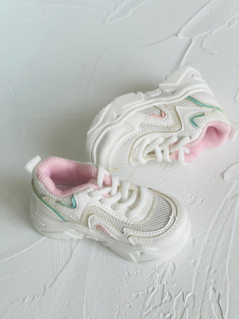 Puede incluir: Zapatillas blancas de malla con ribetes rosas y suela blanca. Las zapatillas tienen un dise&ntilde;o de plataforma gruesa.