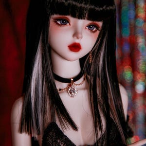 May include: A doll with long black hair with white streaks, wearing a black lace top and a black choker with a rhinestone pendant.