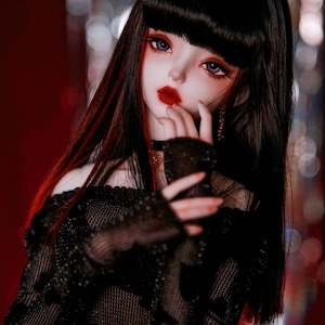 May include: A doll with long black hair with red streaks, wearing a black mesh top with a heart-shaped pendant on a gold chain. The doll has a red lip and blue eyes.