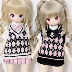 May include: Two dolls with blonde and brown hair wearing pink and black argyle sweaters and skirts. The dolls have pigtails and are wearing white shirts underneath the sweaters.