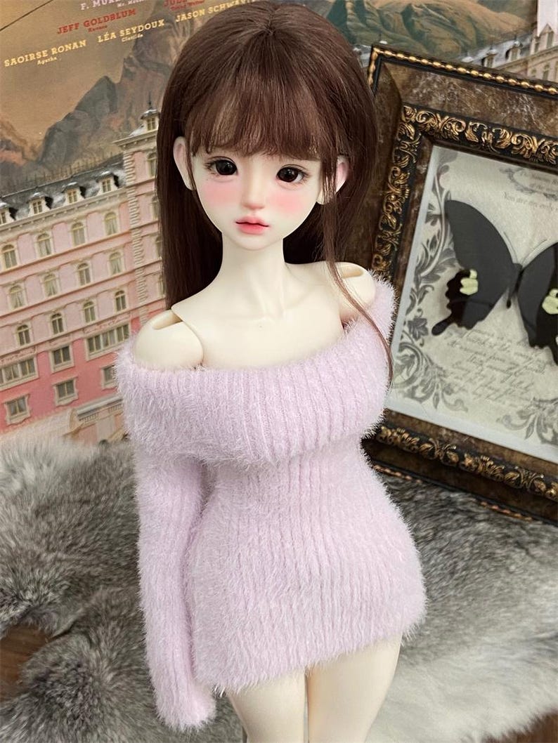 Puede incluir: Una mu&ntilde;eca con un su&eacute;ter rosa claro y peludo de hombros descubiertos. La mu&ntilde;eca tiene el pelo largo y casta&ntilde;o y lleva una falda blanca.