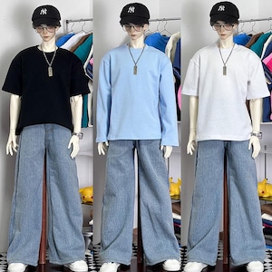 May include: Three mannequins wearing different coloured shirts and blue jeans. The mannequins are wearing black, light blue, and white shirts. All three mannequins are wearing a black and white baseball cap.